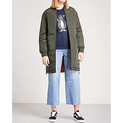 Woman wearing the CHOCOOLATE Reversible Two-Tone Shell Coat with the green side facing outward. Styled with blue jeans, a navy top, and Vans sneakers, this lightweight coat features a stand collar, ribbed trims, and functional pockets, perfect for transitional weather.