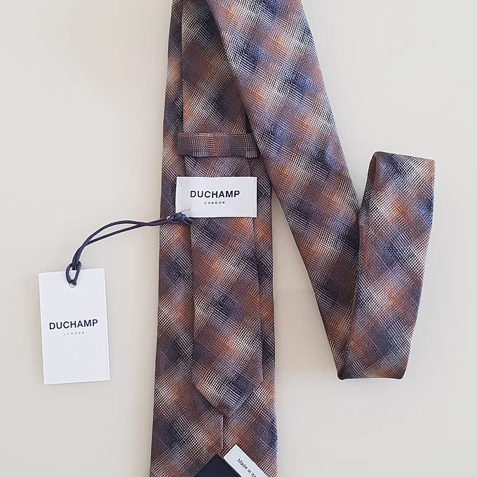 The back of the Duchamp Abstract Check Tie arranged in a zigzag pattern, showcasing the “Duchamp” label stitched onto the tie and the attached tag also bearing the “Duchamp” branding. The image highlights the premium craftsmanship and attention to detail.