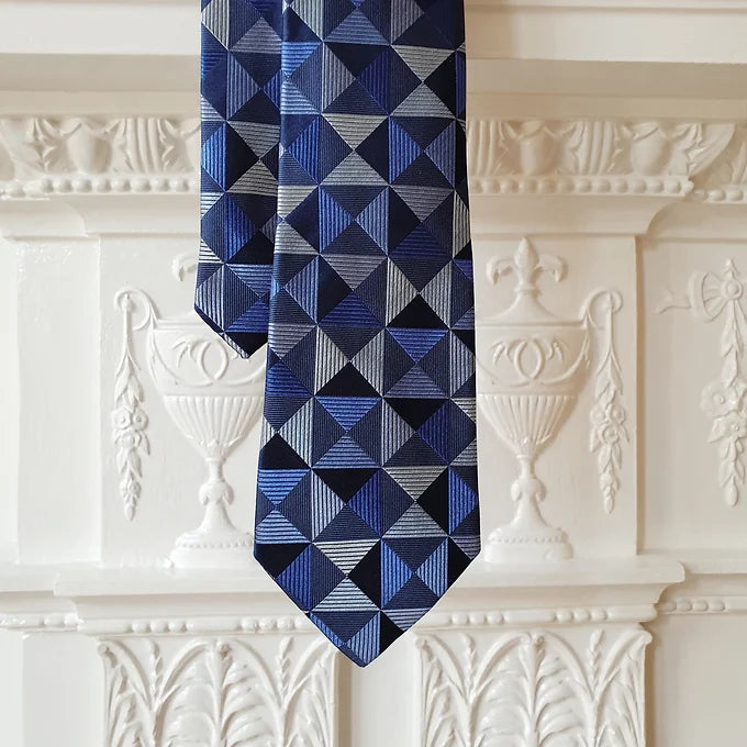 Duchamp London Blue Geometric Silk Tie laid flat, showcasing both the wide blade tip and the narrow tail. The intricate all-over geometric pattern is displayed prominently on the luxurious blue silk fabric.